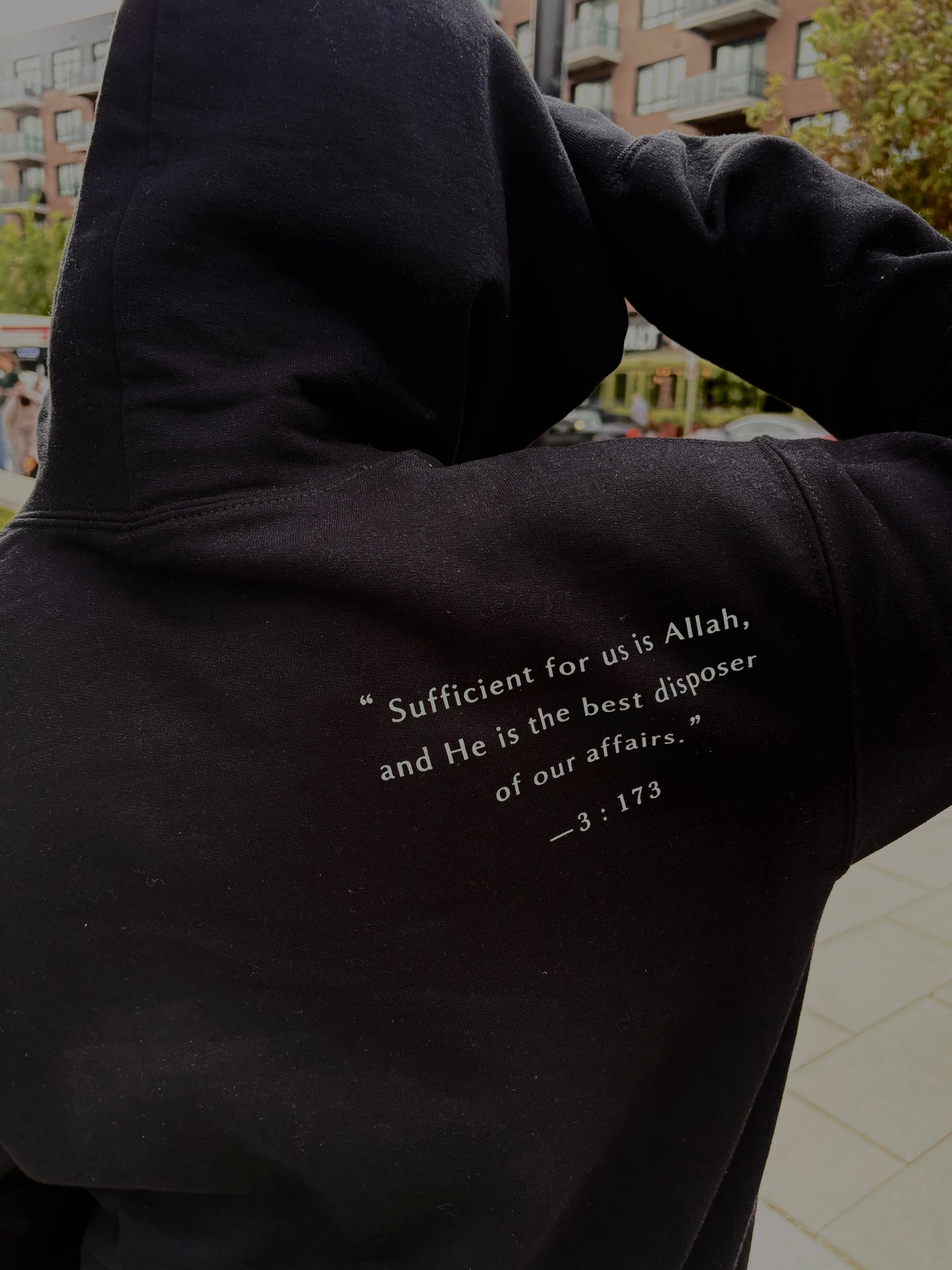 Black hoodie with text on the back, worn by a person, with a blurred background.