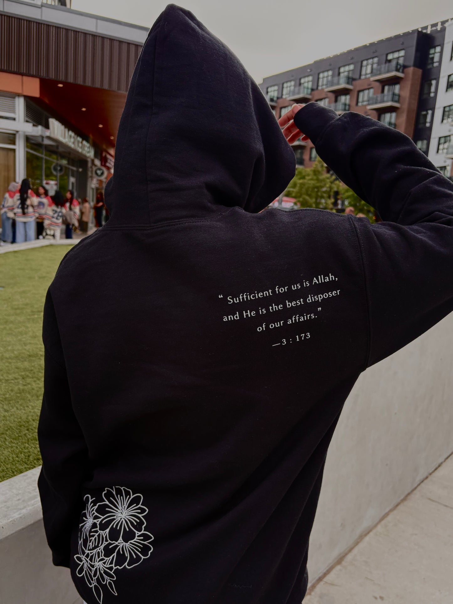Person wearing a black hoodie with text and floral design outdoors.