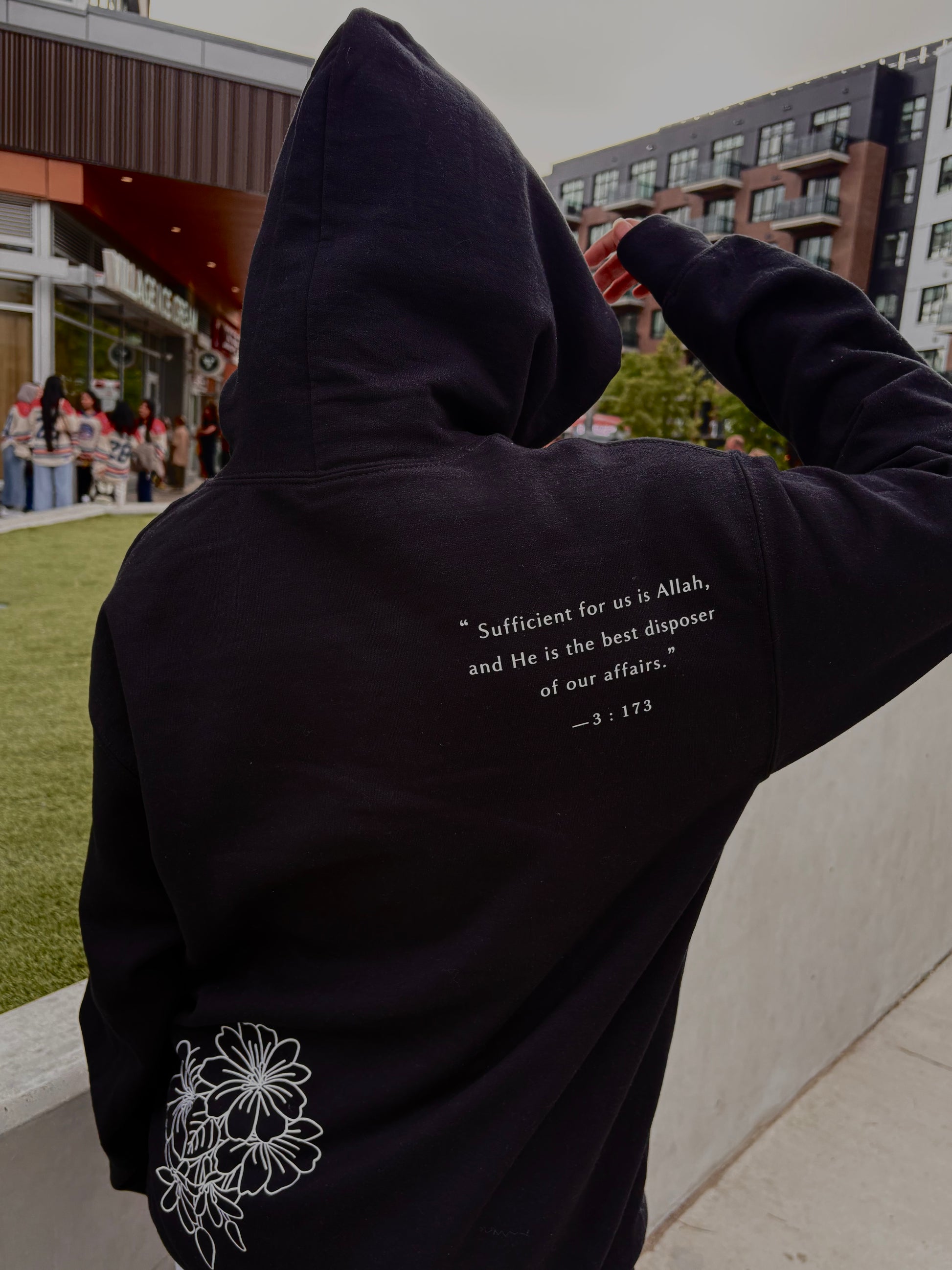 Person wearing a black hoodie with text and floral design outdoors.