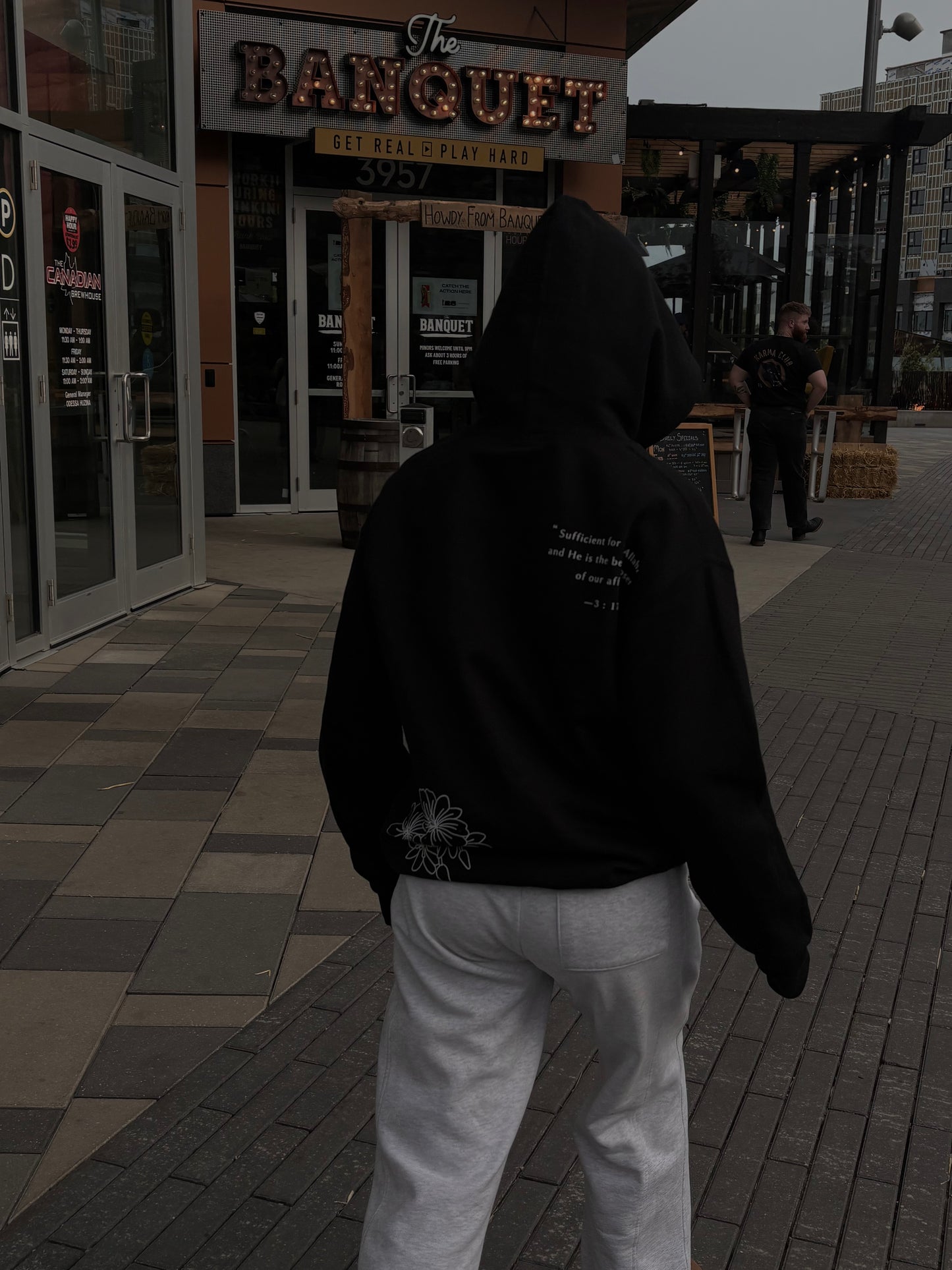 Person wearing a black hoodie with text on the back, walking past 'The Banquet' restaurant.