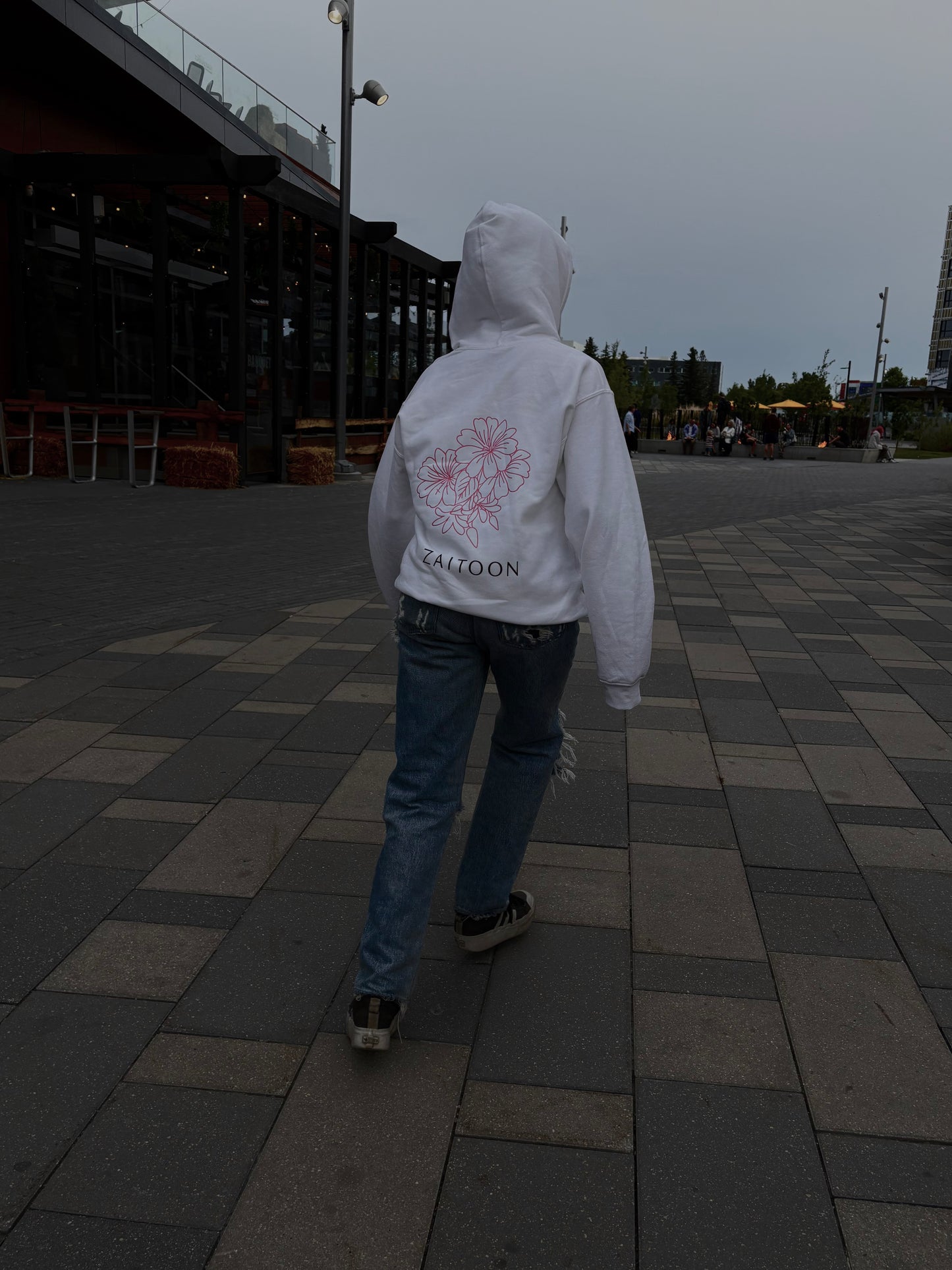 Person wearing a white hoodie with a red logo and text, walking on a paved area.